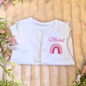 personalised baby sleepsuit made from 100% cotton with an embroiderd name and pink rainbow design on the front chest.