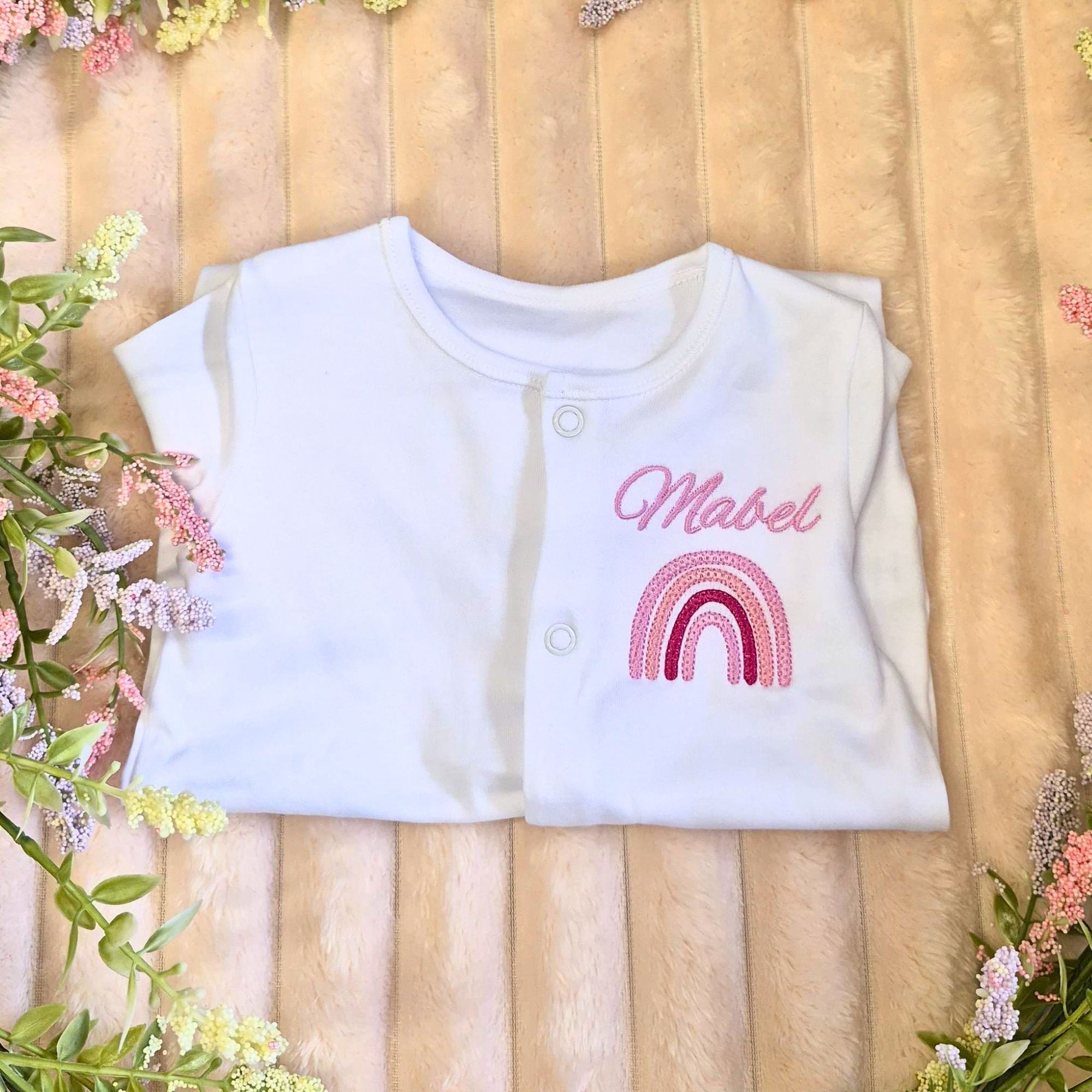 personalised baby sleepsuit made from 100% cotton with an embroiderd name and pink rainbow design on the front chest.